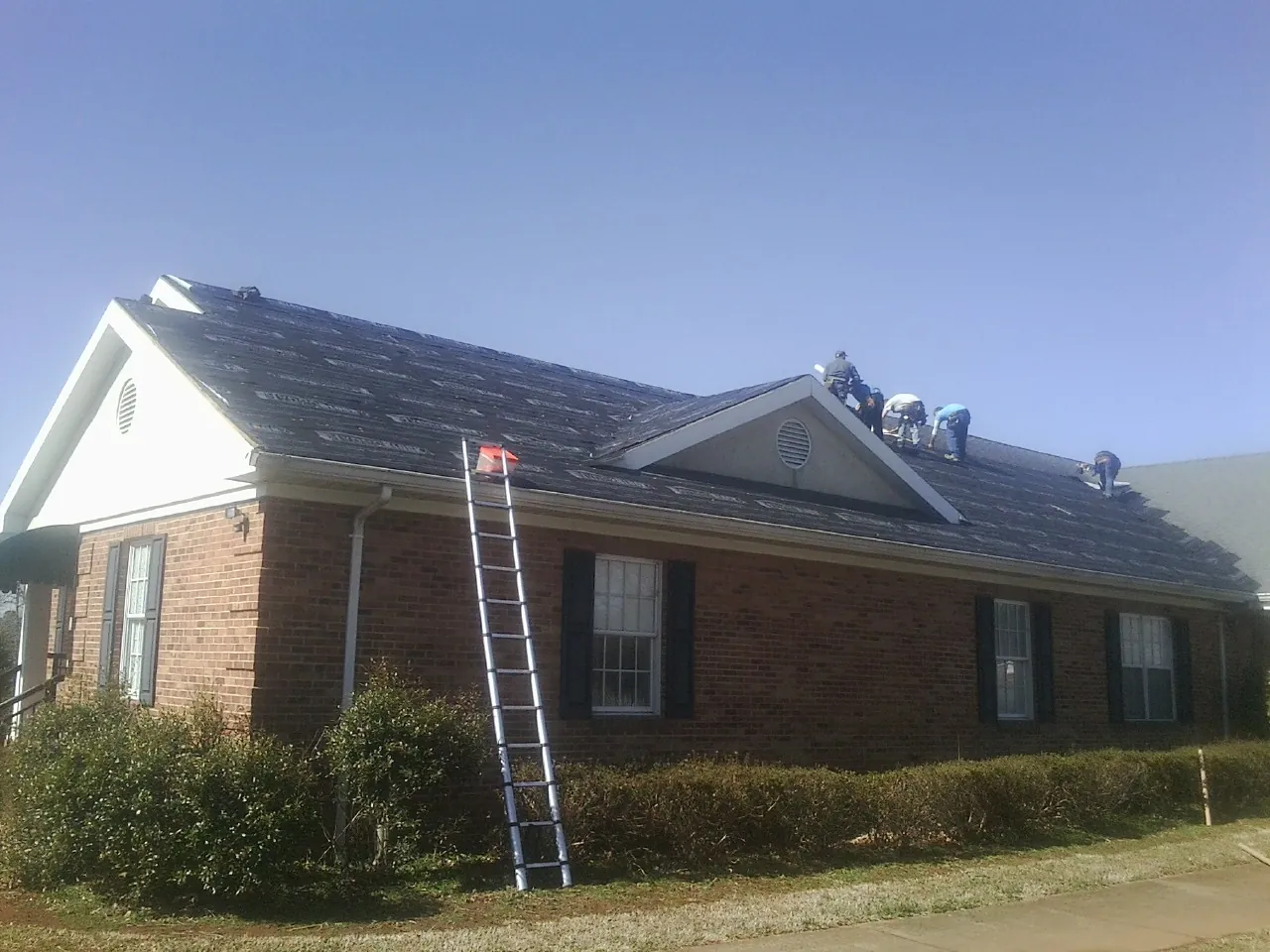 Crew tearing shingles off a brick ranch roof with a ladder set — Emergency Roof Repair work by our crew in Manteo