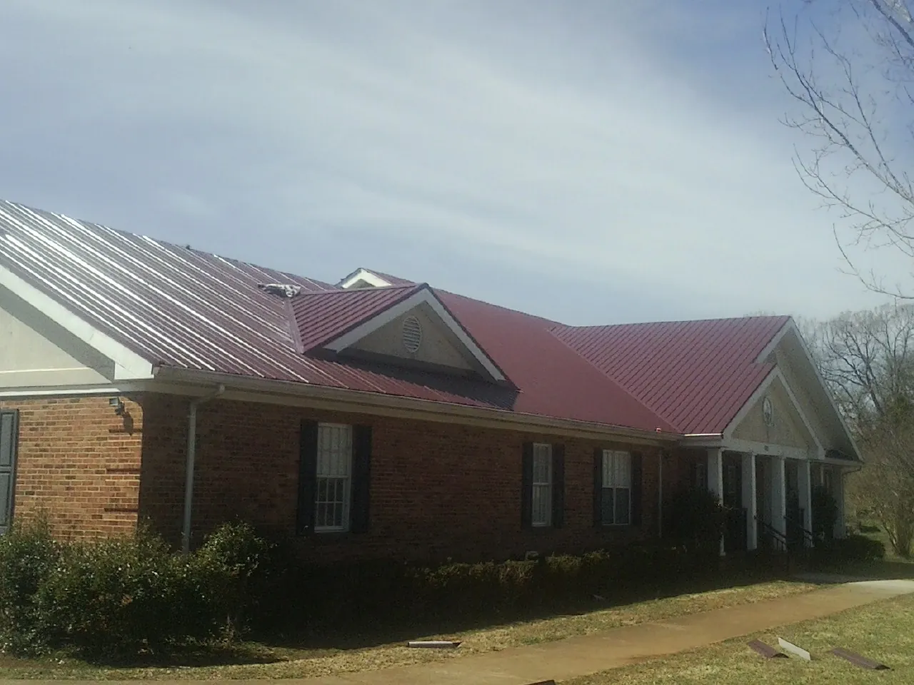 Red metal roof with gabled entries on a long brick building, from a Hail Damage Roof Repair job in Manteo