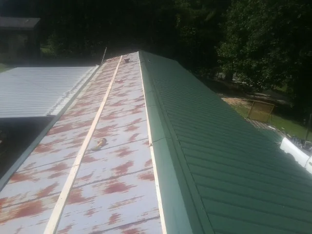 Old rusted panels beside newly installed green metal roofing — Wind Damage Roof Repair by Roofing Brothers in Manteo