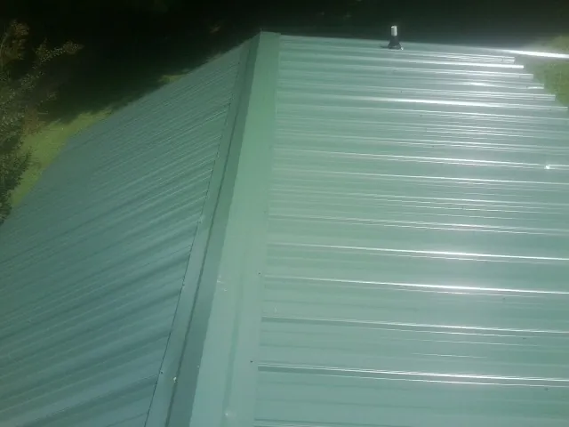 New green metal panels meeting at the ridge of a roof — Flat Roof Repair work by our crew in Manteo