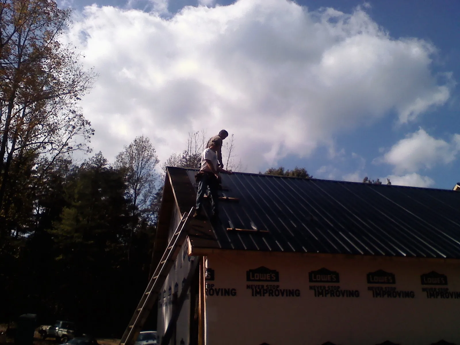 Roofer fastening dark metal panels high against a cloudy sky, from a Roof Inspection job in Manteo