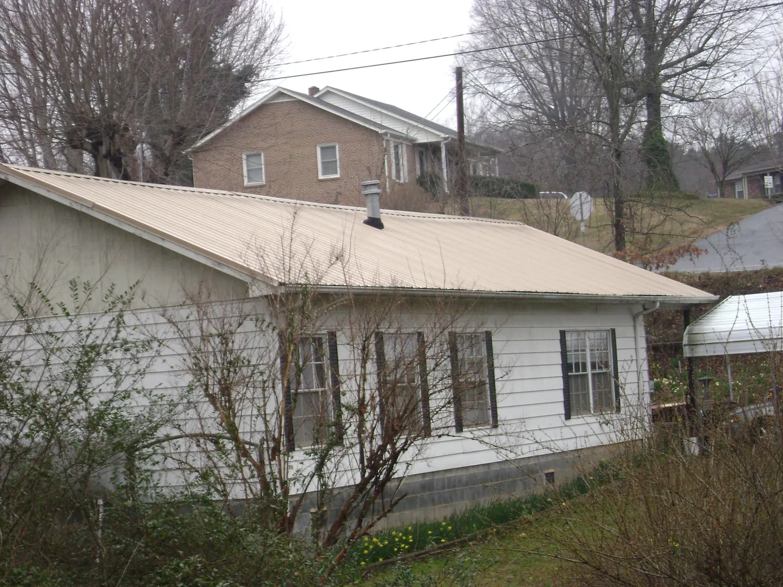 Tan metal roof on a white sided house set into a hillside — Commercial Roofing by Roofing Brothers in Manteo