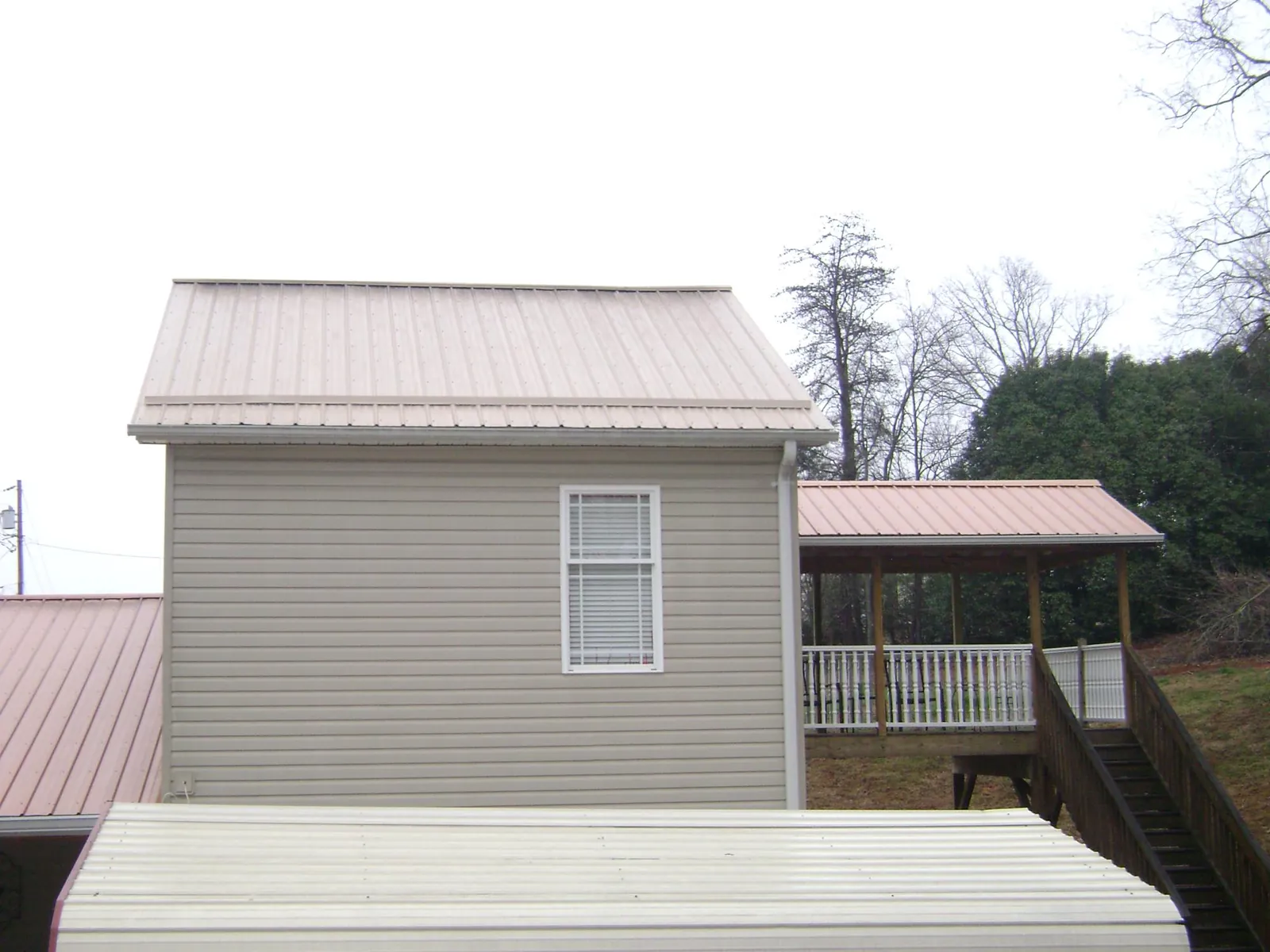 Tan metal roofs on a two story addition and attached porch, from a Roof Replacement job in Manteo